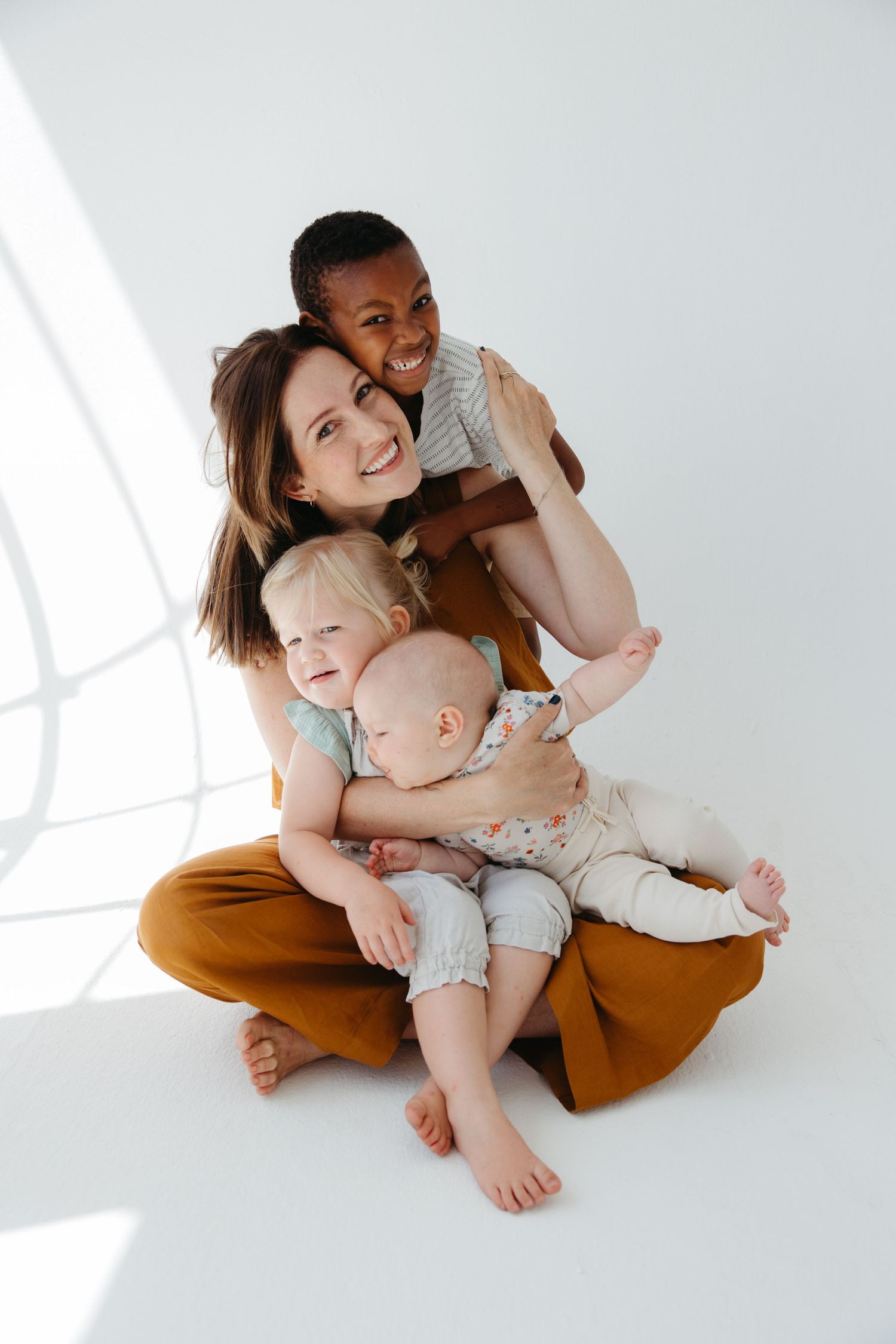 A joyful family plays and laughs together on a bright white floor.