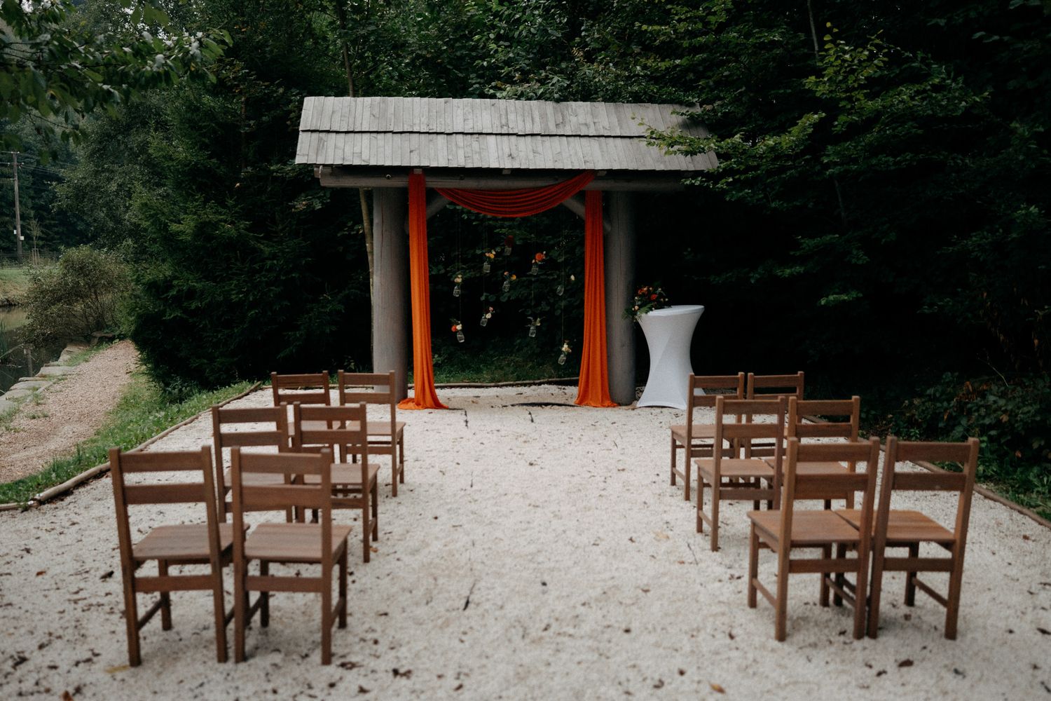 Wooden chairs arranged in rows facing a small red and orange arch for an intimate outdoor forest wedding ceremony.