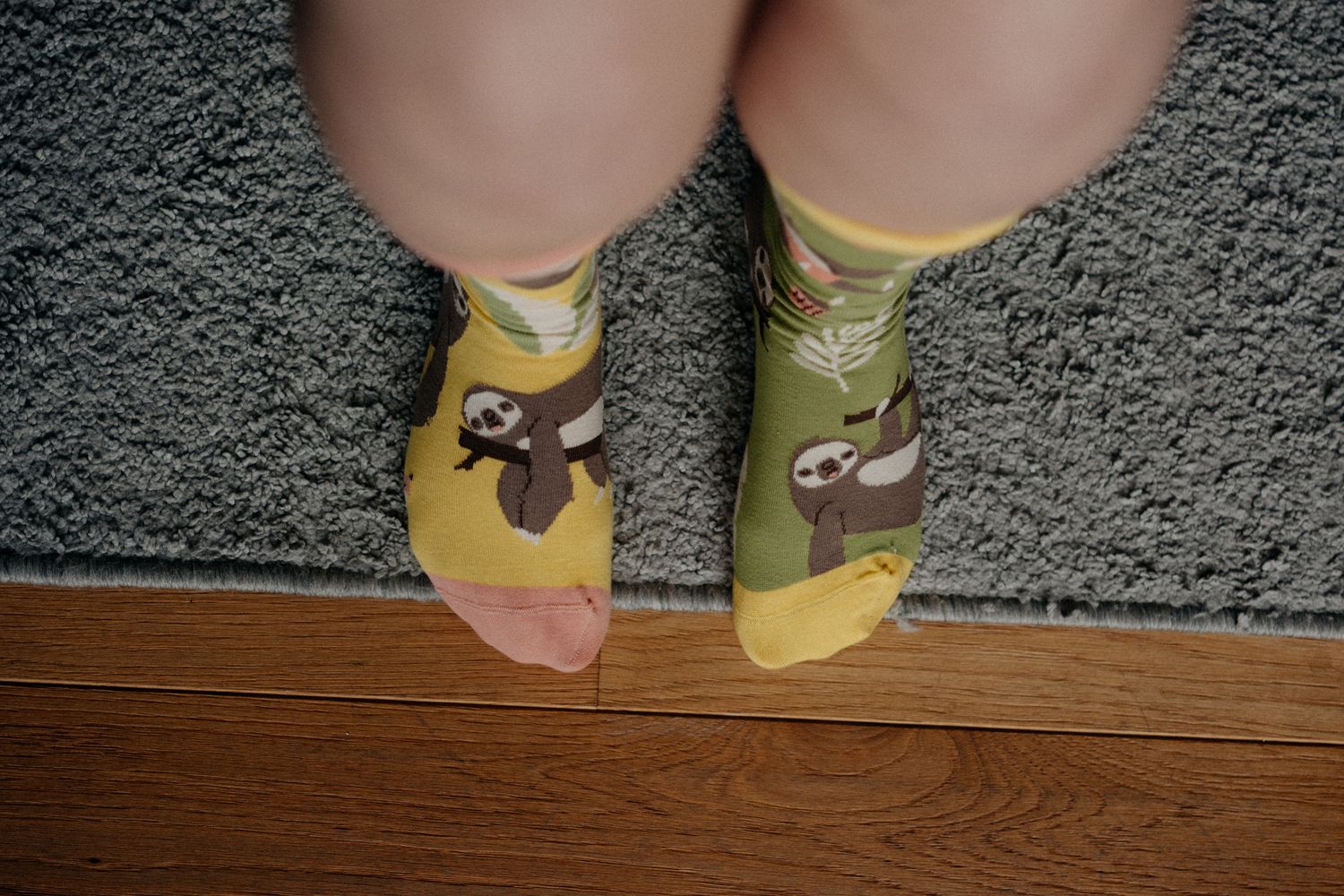 Cute sloth-themed socks on feet against grey carpet.