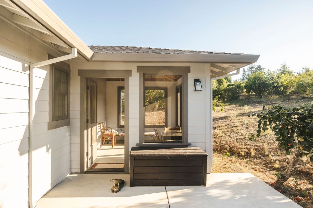 Modern ranch-style home exterior with white walls, solar panels, and a covered patio area surrounded by desert landscaping.