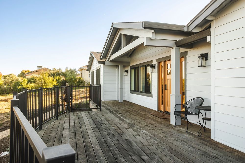 Modern deck and patio area of a residential home with white siding and black railings at sunset.
