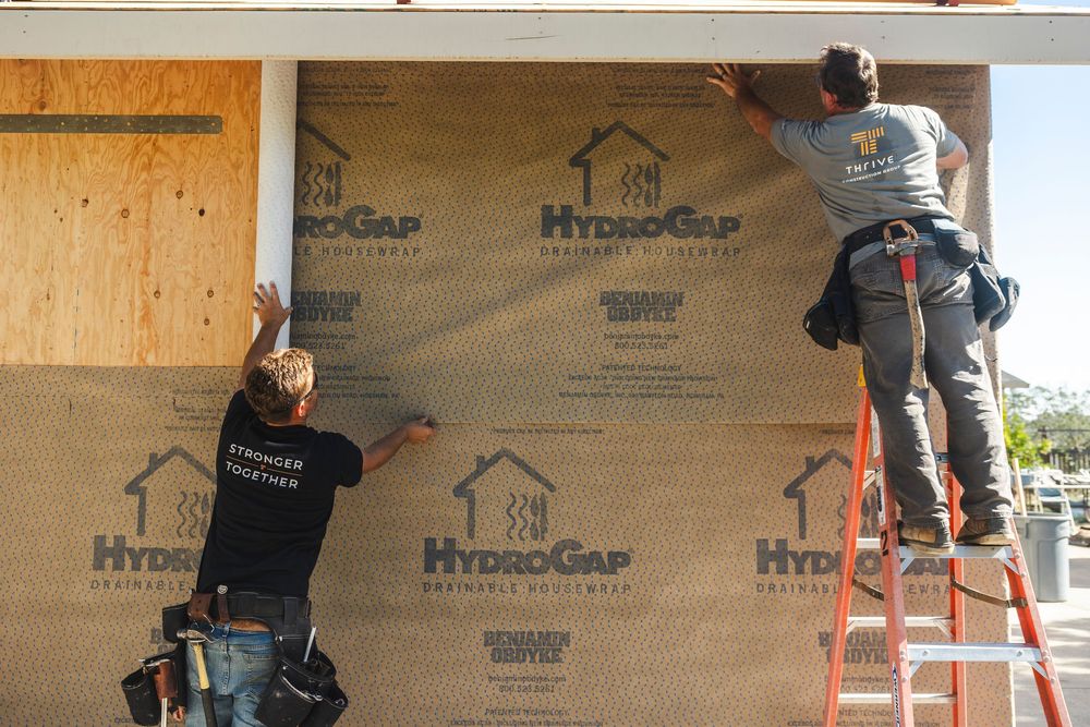 Construction workers installing HydroGap water-resistant barrier on exterior wall sheathing during home build.