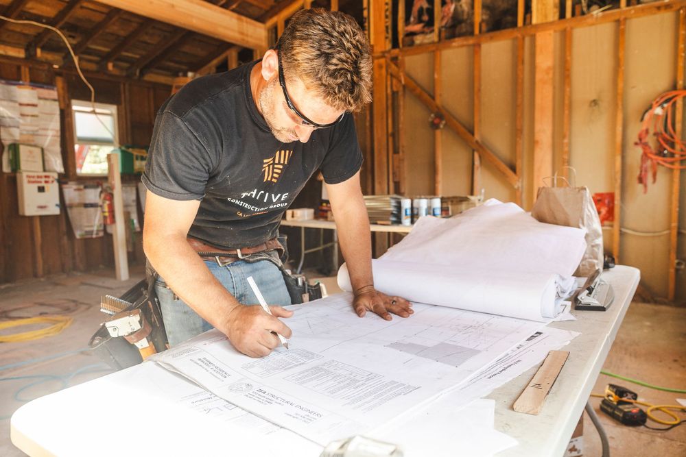 Construction workers review architectural blueprints and plans on a wooden workbench in an unfinished building.