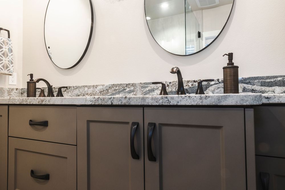 Elegant bathroom vanity with dark wood cabinets, granite countertop, and oil-rubbed bronze fixtures against white walls.