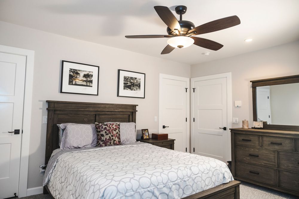 Modern bedroom interior with white walls, ceiling fan, and dark wood furniture.