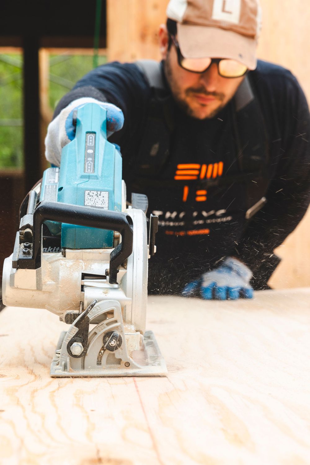Close-up of blue power saw tool with worker wearing Thrive branded shirt in background.