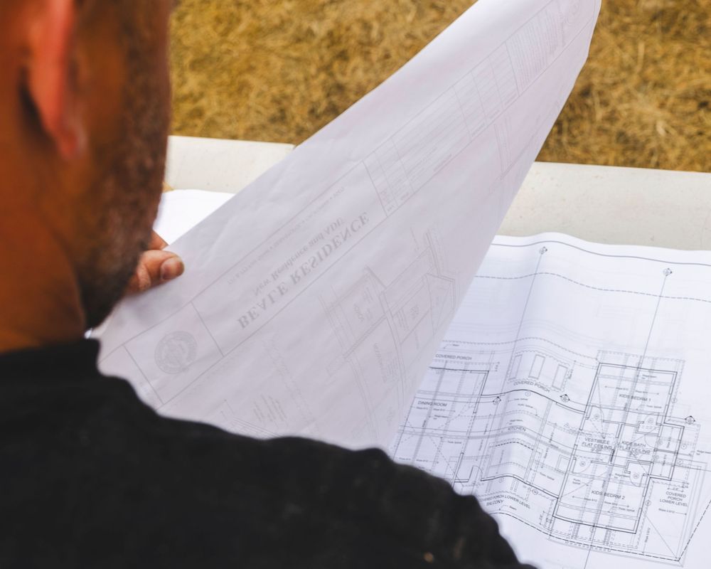 Overhead view of architectural blueprints being reviewed on a dark surface.