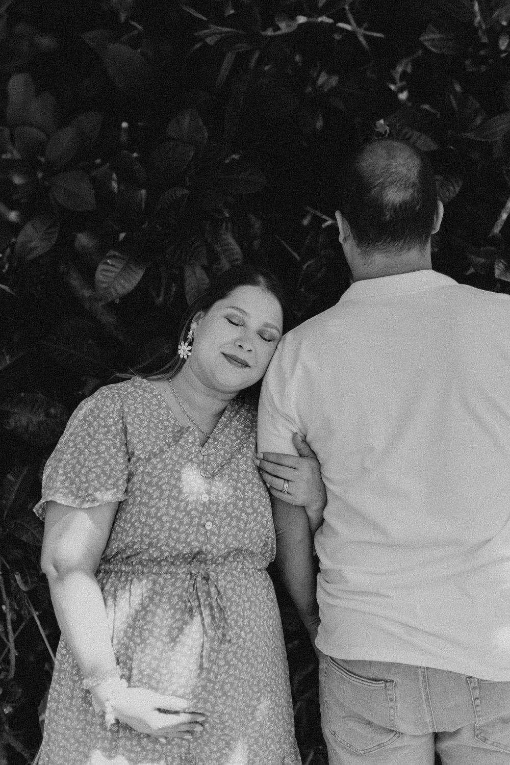 A couple embraces in a black and white photo against foliage backdrop.