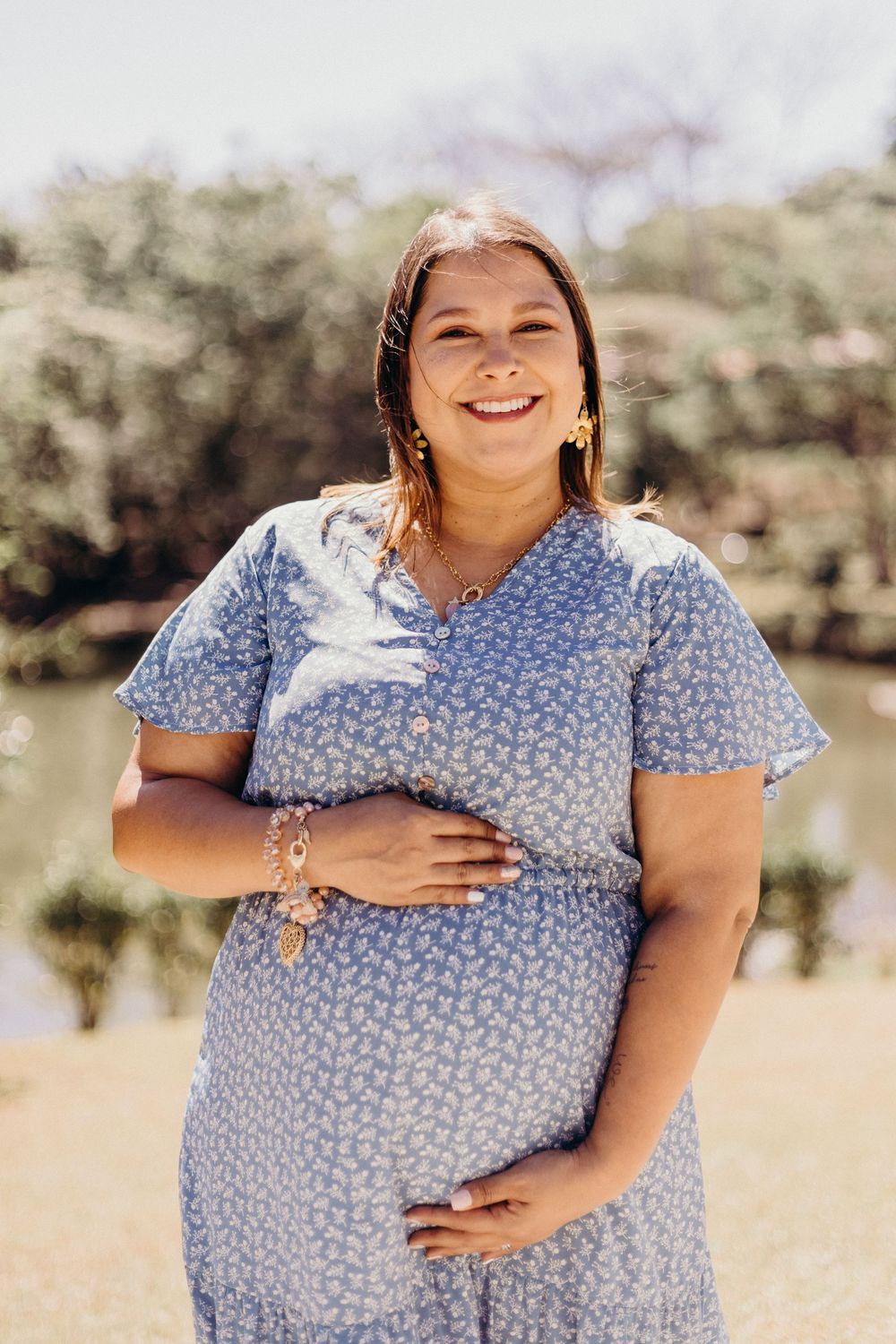 Maternity photo series showing woman in blue floral dress cradling baby bump outdoors in natural lighting.