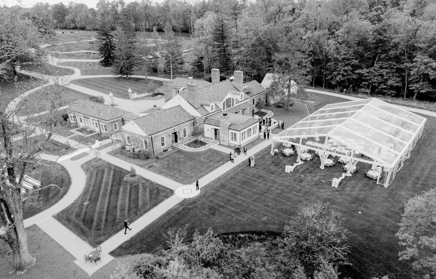 Aerial black and white panoramic view of a suburban neighborhood with houses and winding roads surrounded by trees.