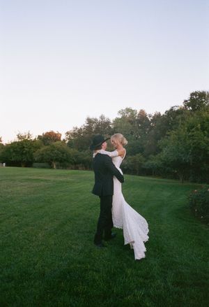 A couple dances together on a grassy field at sunset creating a romantic silhouette against the evening sky.