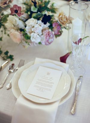 Elegant wedding table settings with white plates, crystal glasses, and delicate floral arrangements in soft pastel colors.