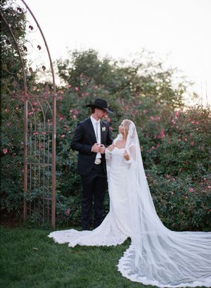 Garden wedding scene with rustic metal archway and blooming pink roses in the background.
