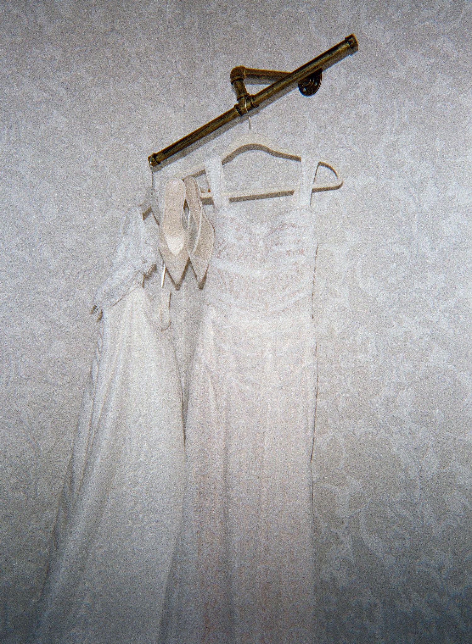 Several white bridesmaid dresses hanging on wooden hangers against a textured grey wall.