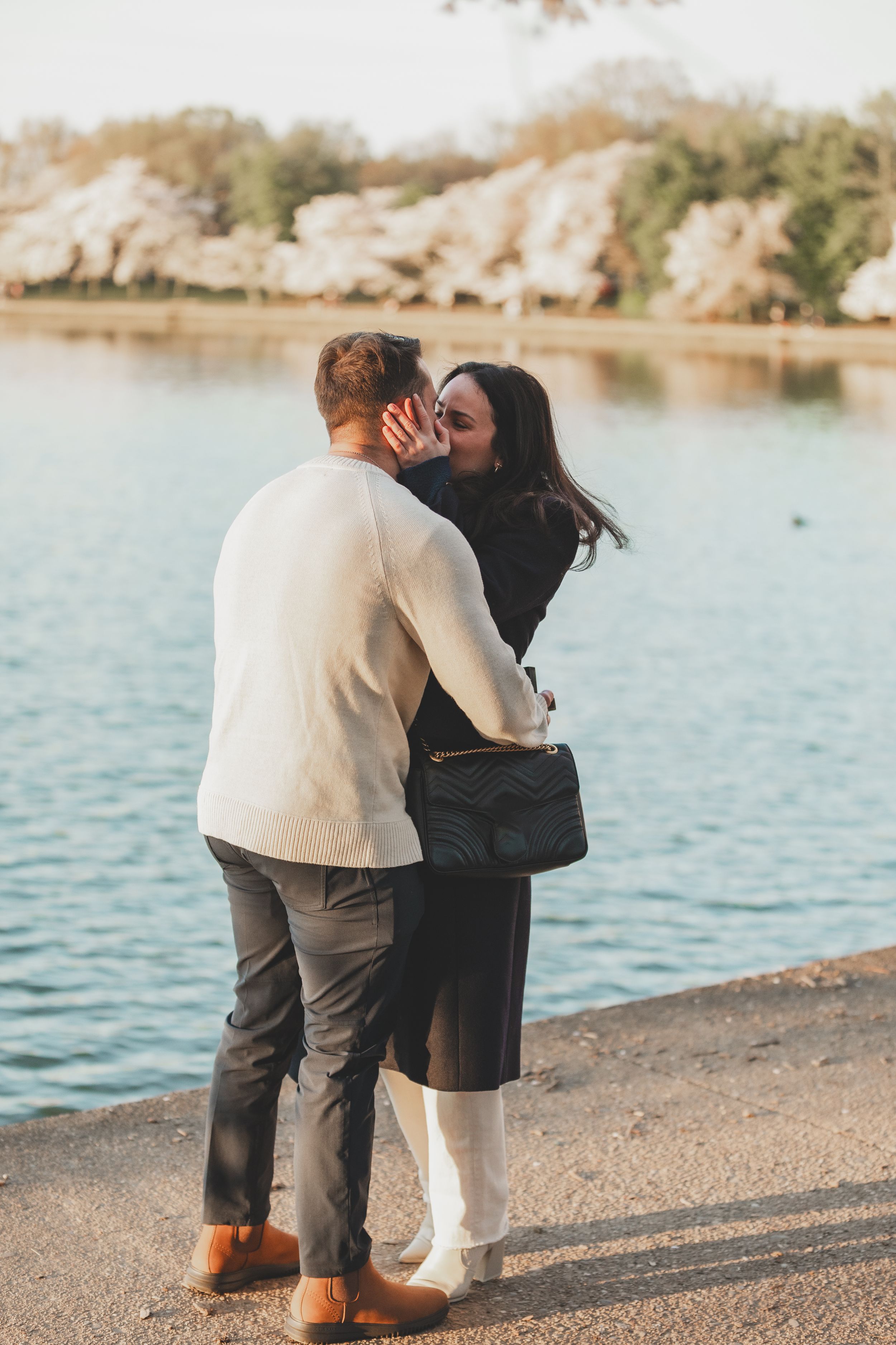 a newly engaged couple in winter clothing share a sweet moment by a serene lake of the tidal basin