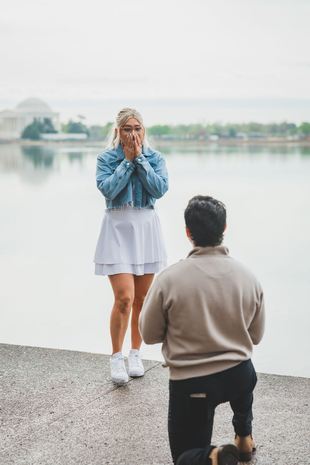 A romantic proposal scene at the Jefferson Memorial with the Tidal Basin in the background on an overcast day.