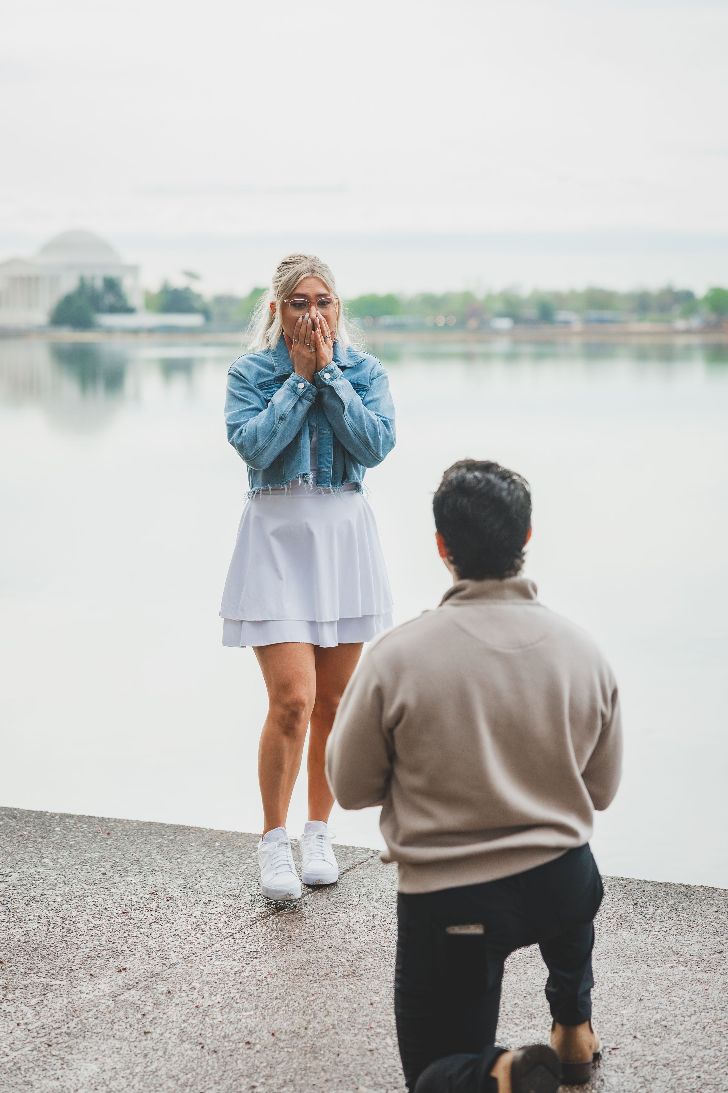 A romantic proposal scene at the Jefferson Memorial with the Tidal Basin in the background on an overcast day.