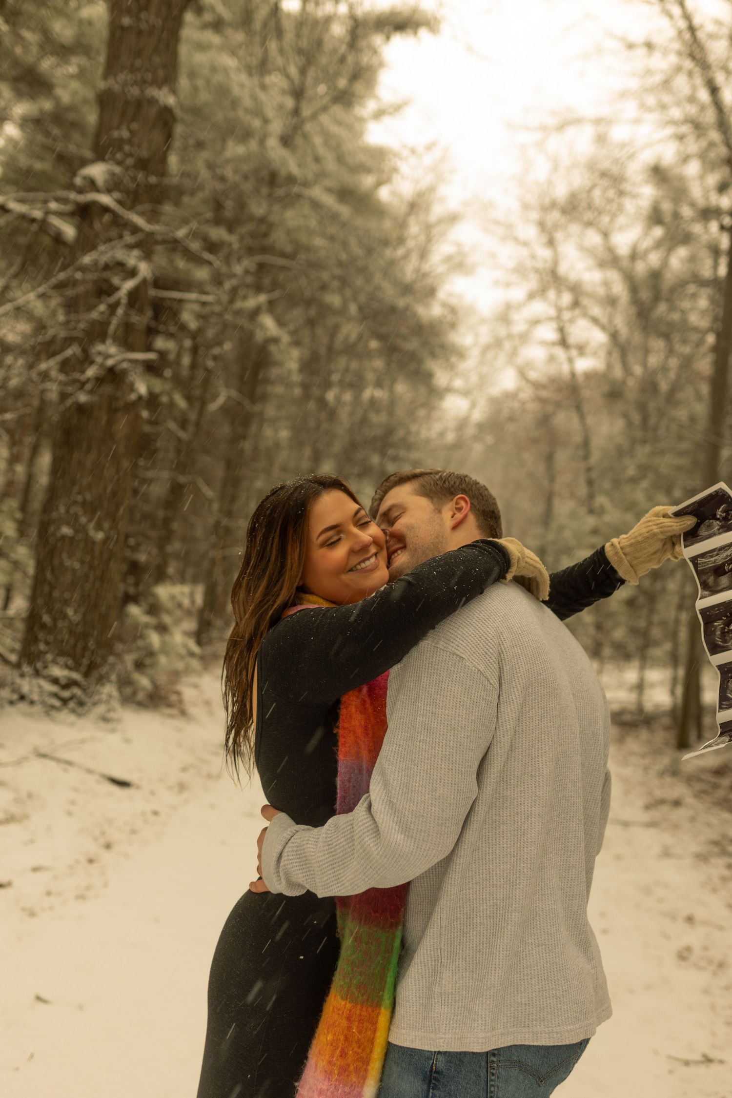 A couple shares an intimate moment in a snowy forest landscape with a dreamy, soft focus effect. Creative Art By Bree LLC