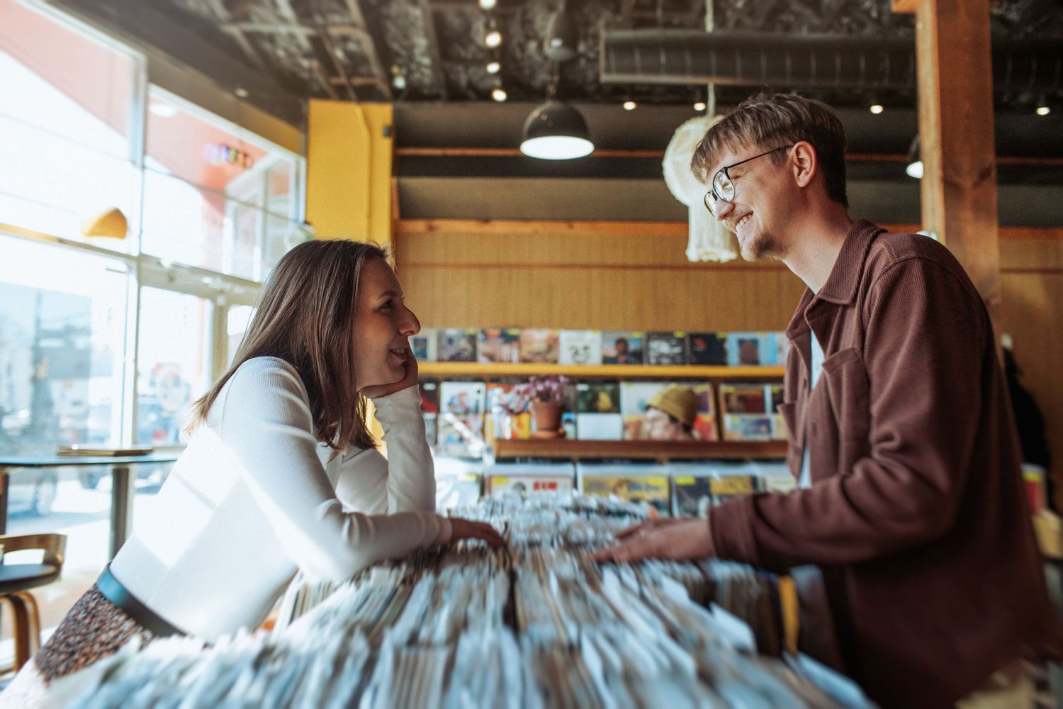 Two people browse through vinyl records together at a music store while engaged in conversation. Indianapolis, Indiana engagement session.