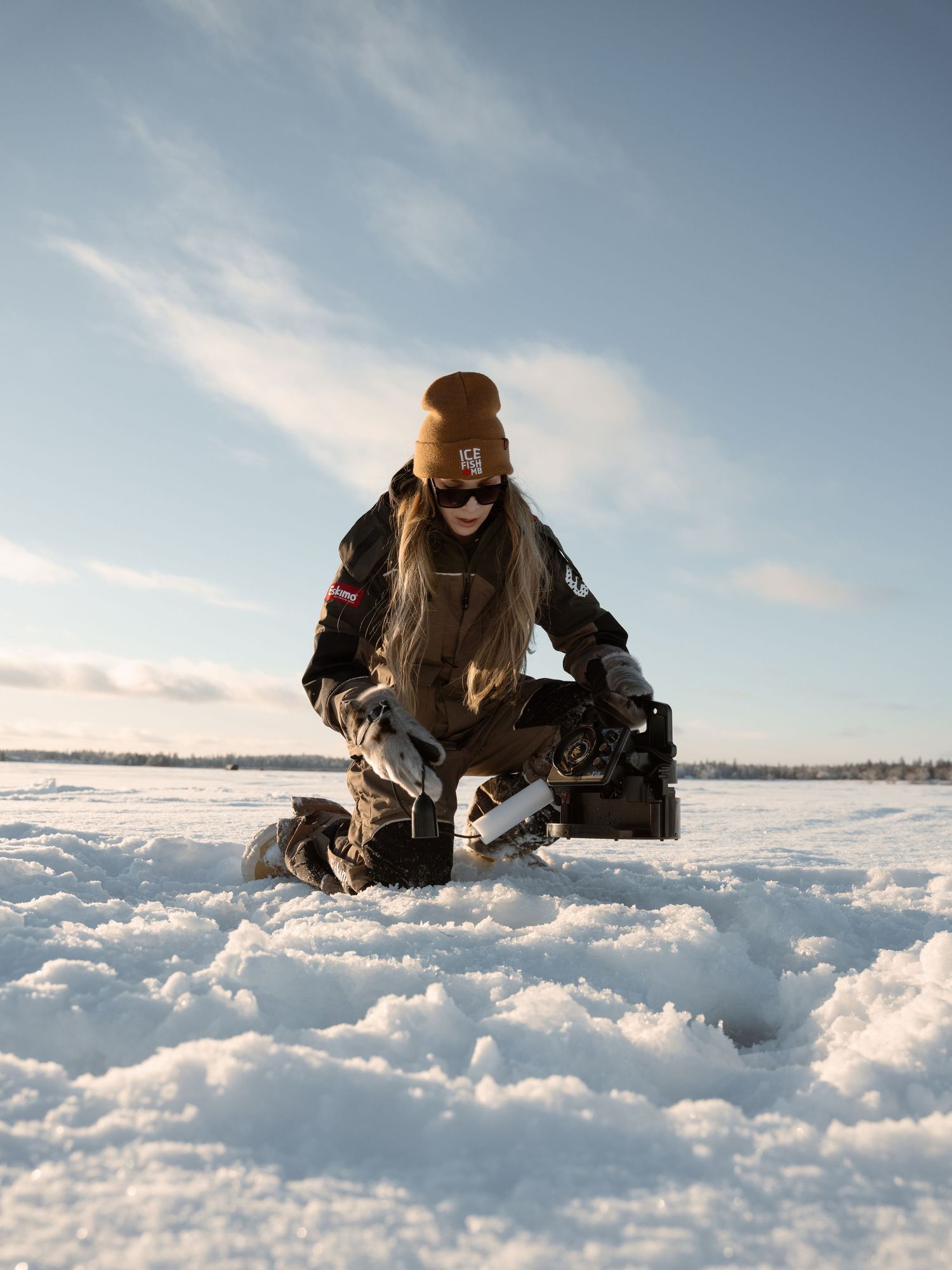 Person ice fishing on a frozen lake during a bright winter day with snowy conditions.