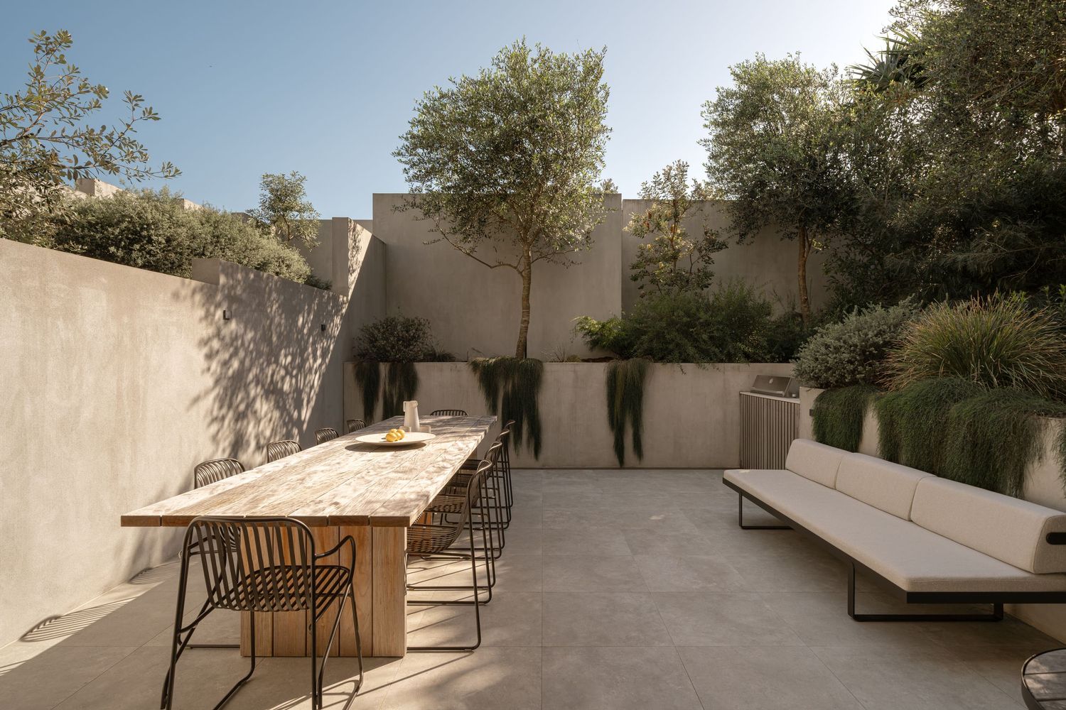 Outdoor terrace with wooden benches and white walls surrounded by lush greenery and natural landscaping.