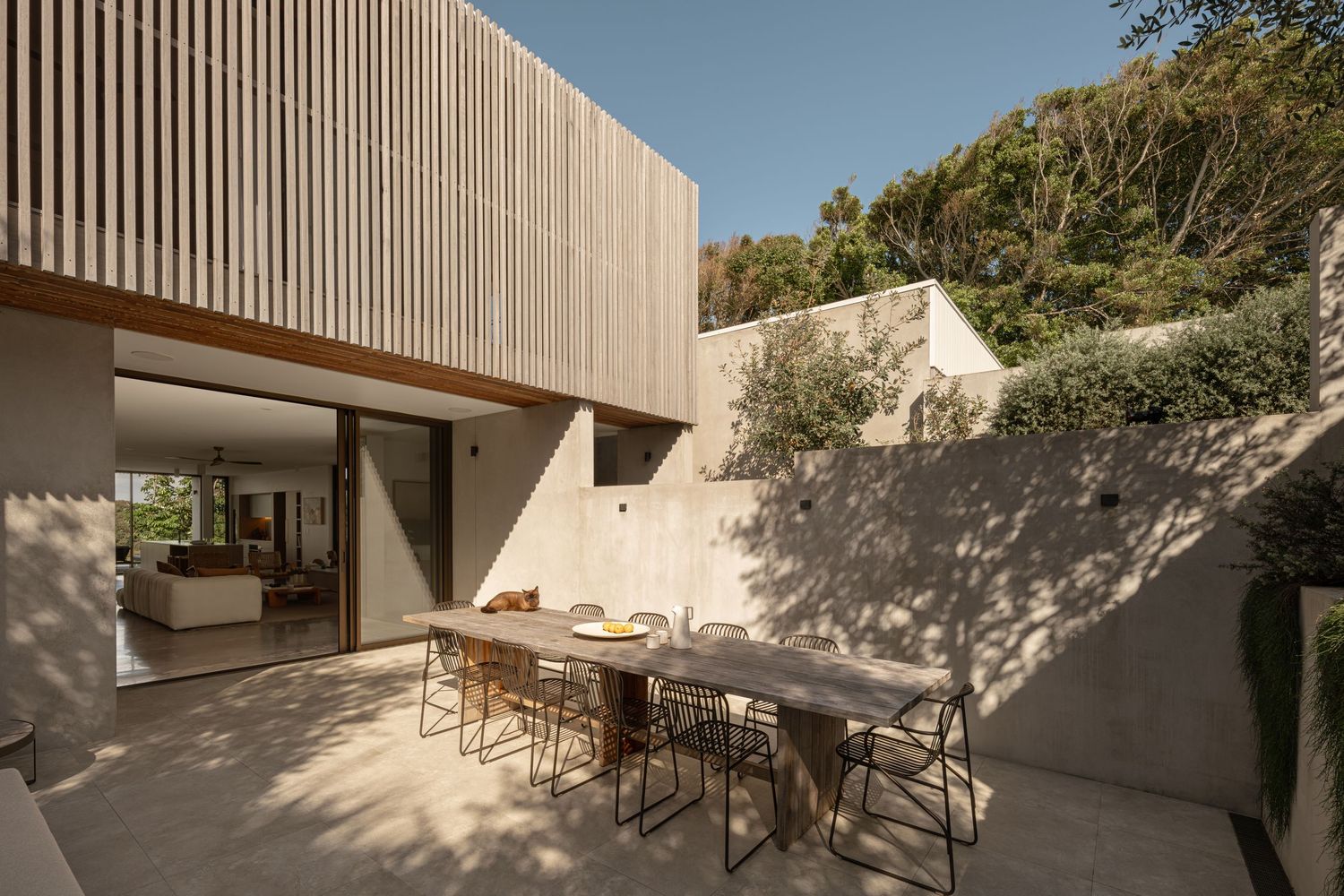 Modern outdoor dining area with wooden slat wall and concrete patio featuring contemporary furniture and clean lines.