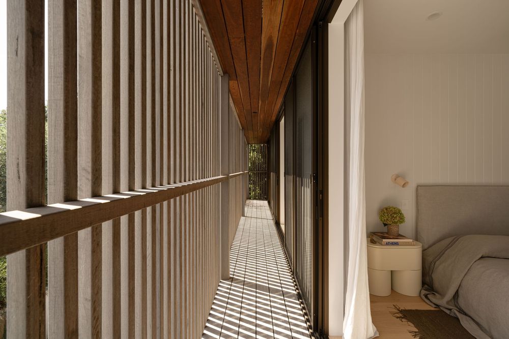 Modern bedroom interior with vertical white slats, wooden ceiling beams, and natural light streaming through windows.