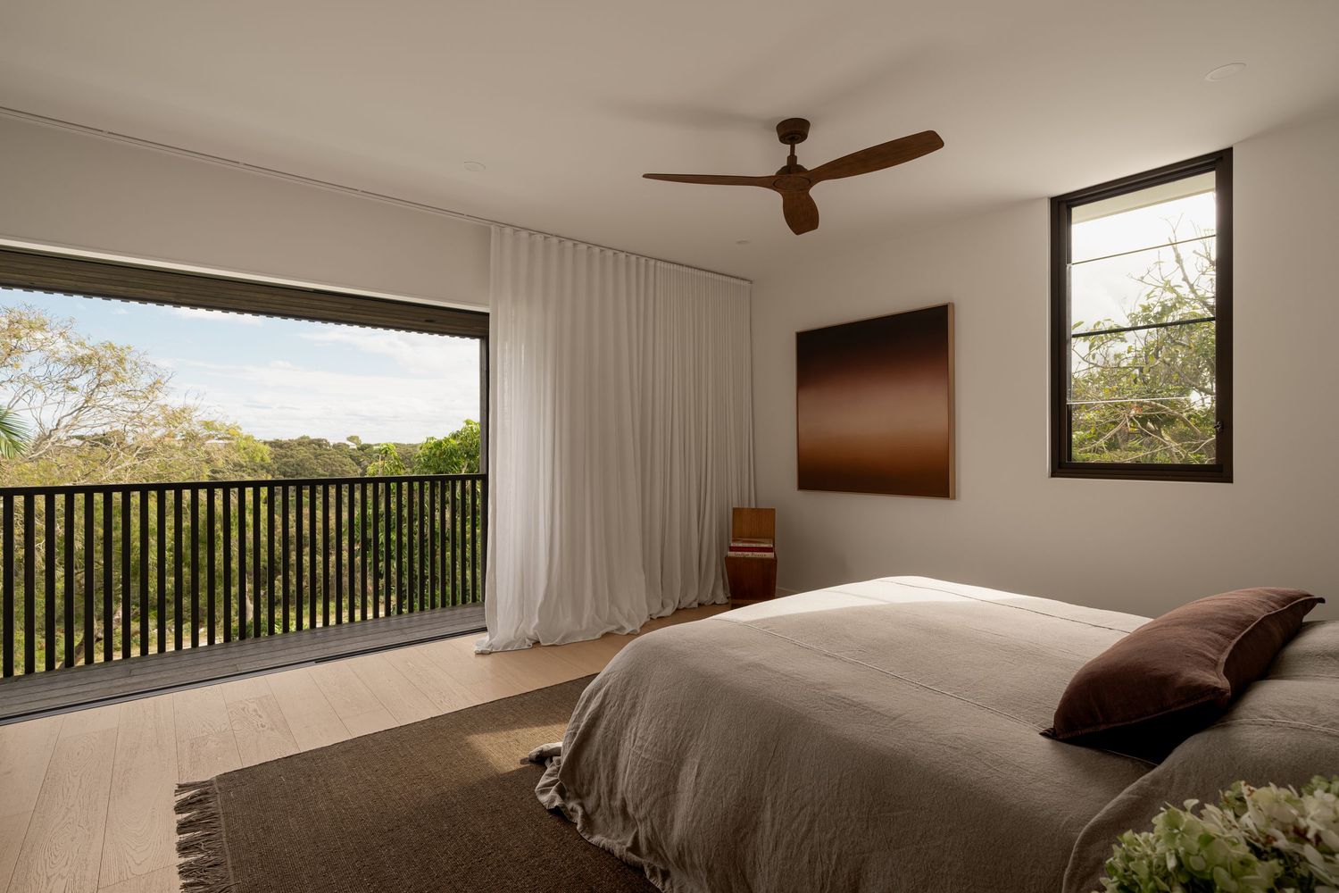 Modern minimalist bedroom with white walls, ceiling fan, and large window offering scenic mountain views.