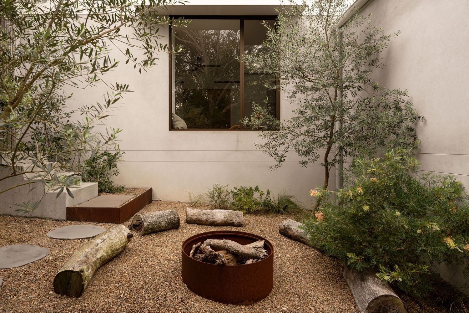 A modern landscaped garden courtyard with metal planters, gravel paths, and natural vegetation against white walls.