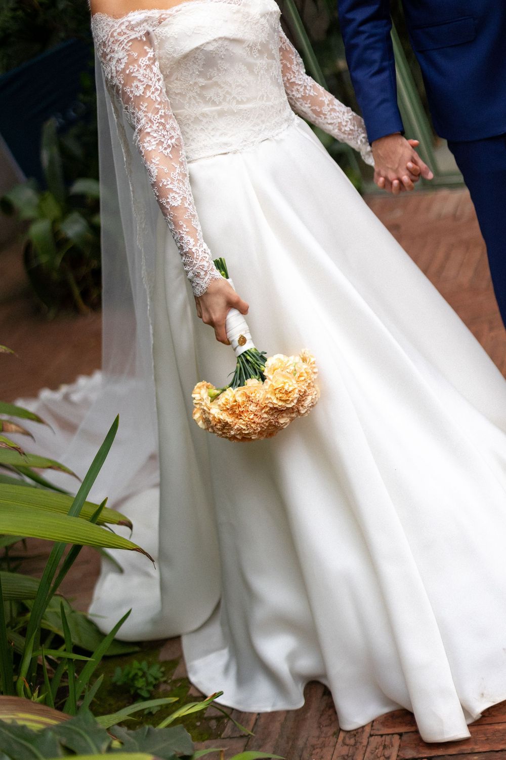 Close-up details of an elegant white wedding dress with lace sleeves and a bouquet of yellow flowers.