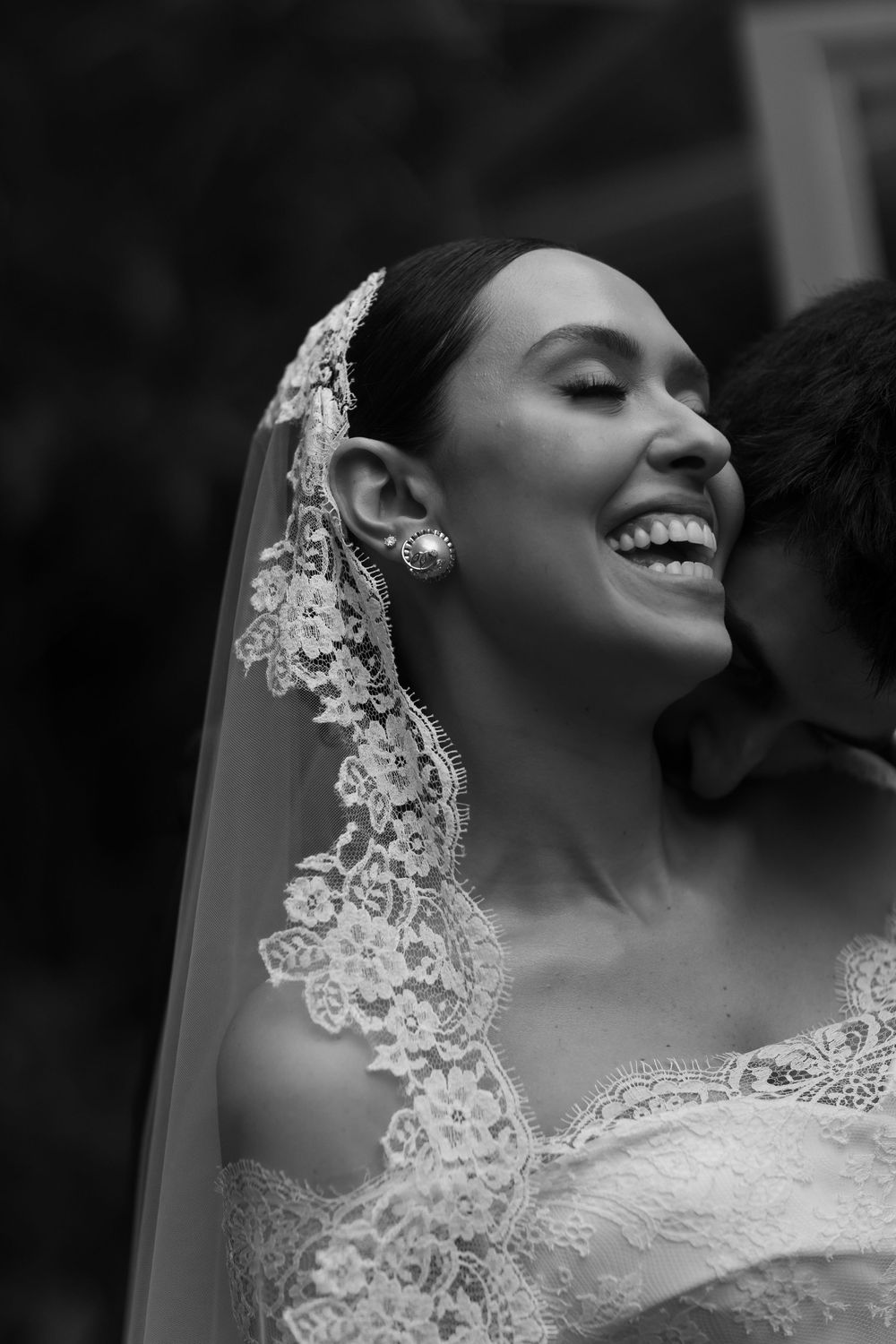 Close-up black and white portrait showing delicate lace details of a wedding veil and dress.