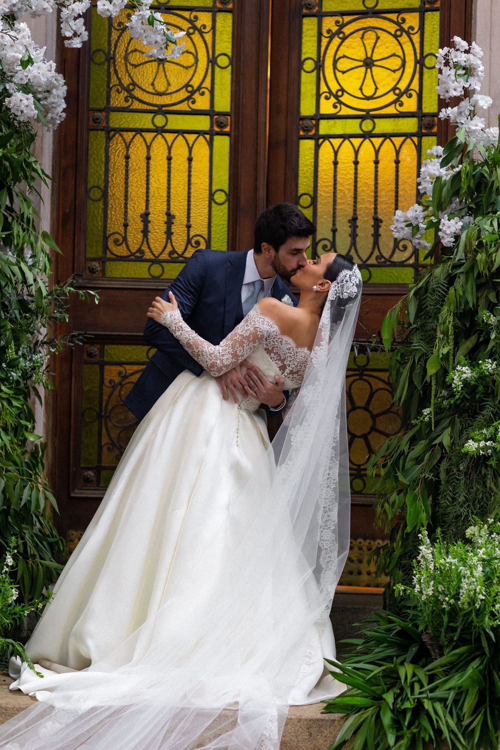 Elegant wedding scene against ornate yellow stained glass windows with floral decorations.