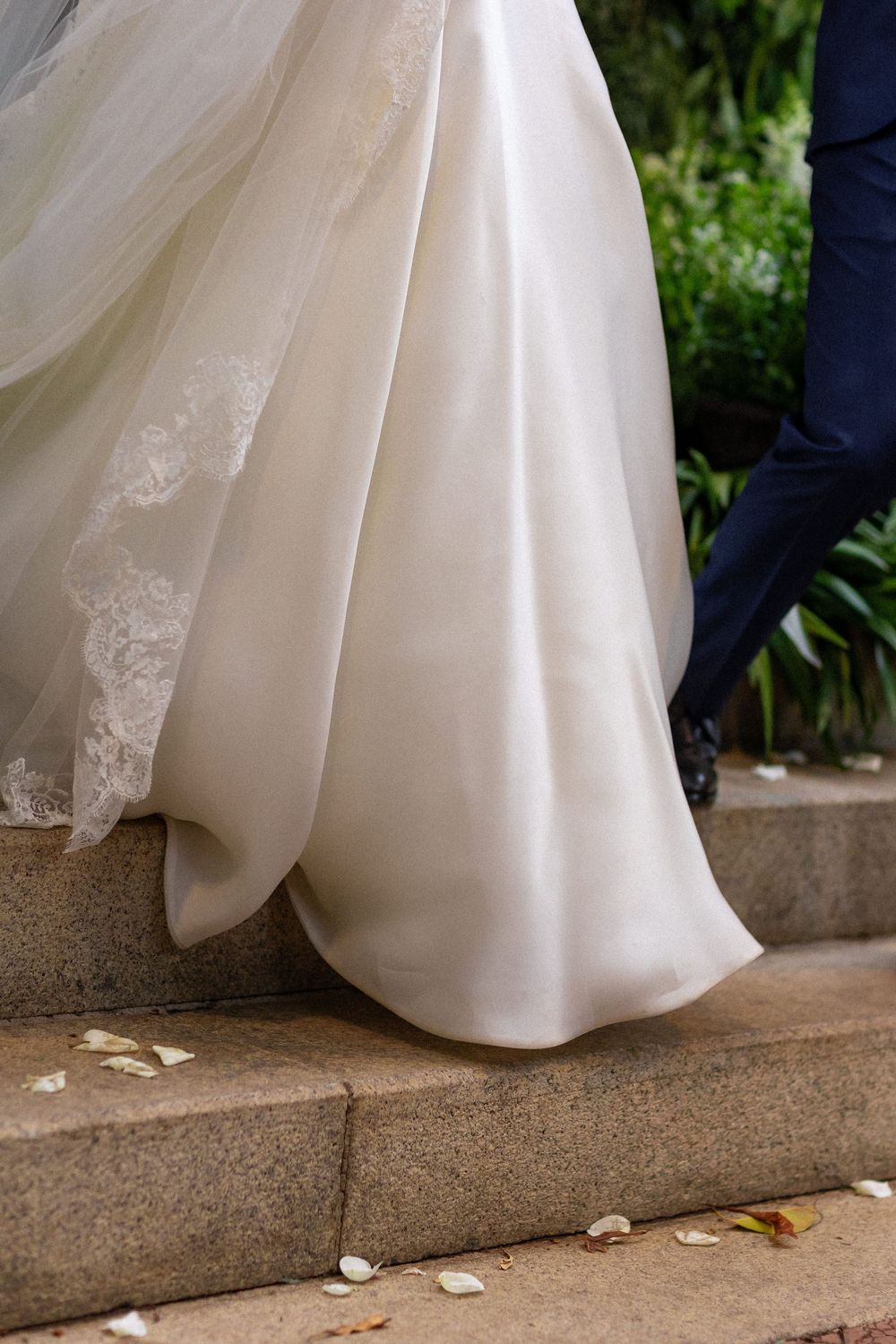 Close-up sequence of a white wedding dress hem trailing along stone steps with scattered rose petals.
