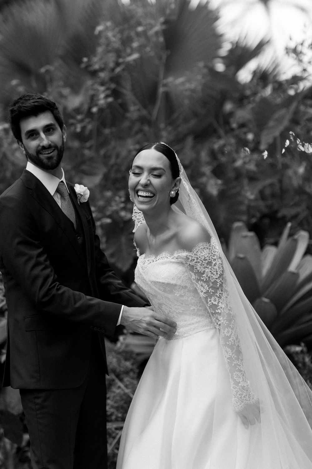 A joyful black and white wedding photo captured in a lush tropical garden setting.