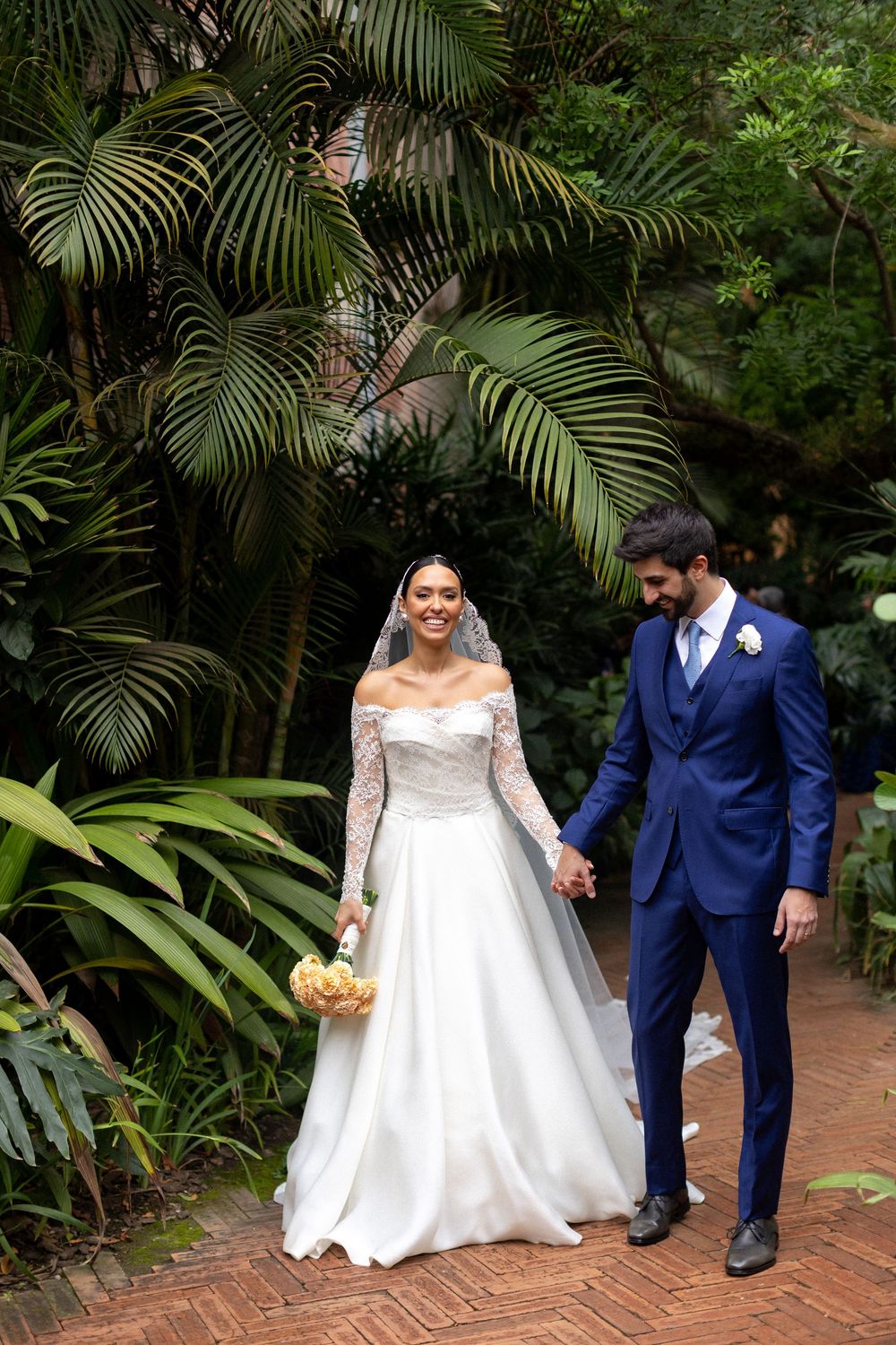 Newlyweds sharing a romantic moment on a garden path with palm trees in the background.