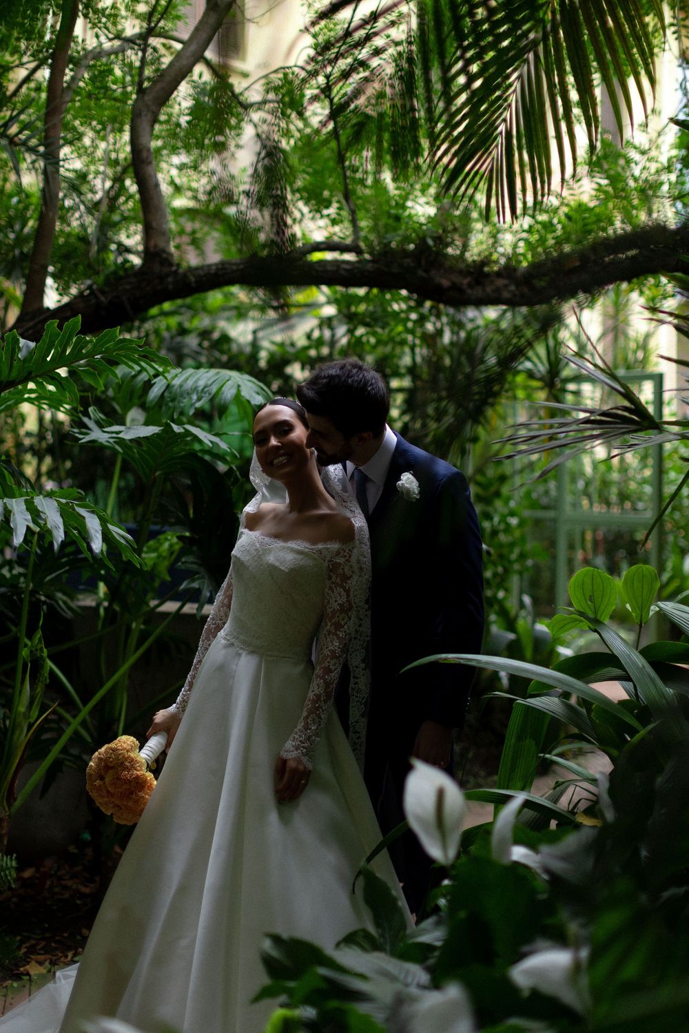 Intimate wedding portrait among tropical palm fronds and garden greenery.