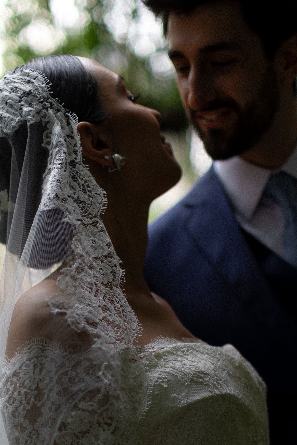 Intimate moment between newlyweds captured in soft natural lighting with lace veil detail.