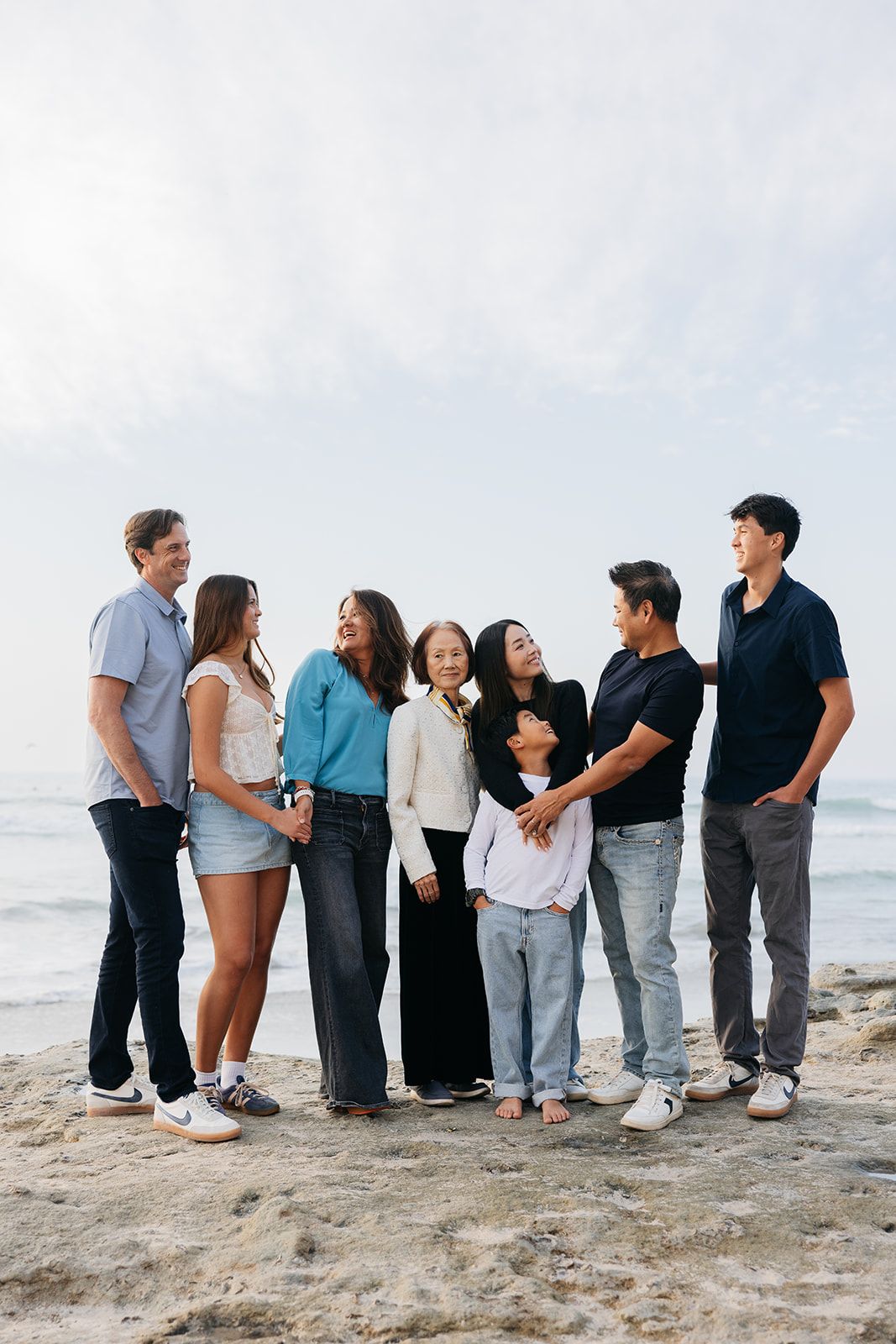 A group of people standing together in a line on a sandy beach, photographed from behind against an ocean backdrop.