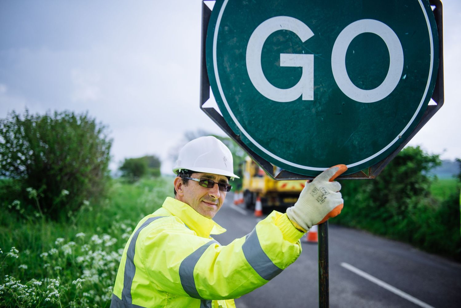 Worker in high visibility gear installing green traffic signs on a pole.