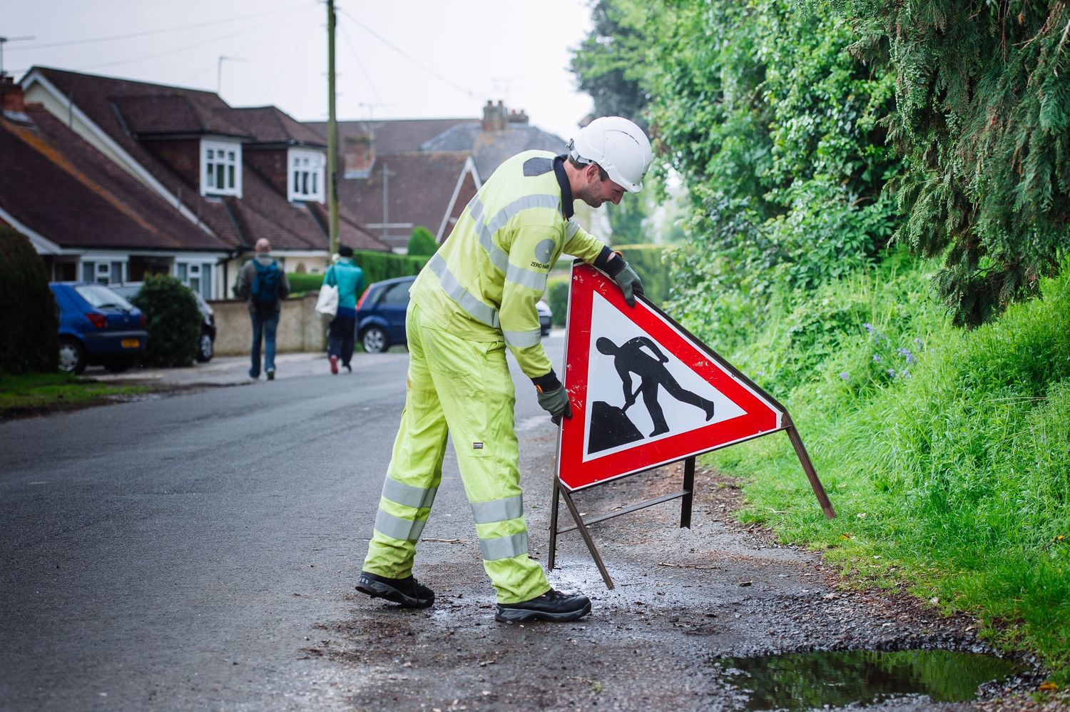 Maintenance worker in safety vest working on street signs in a residential area.