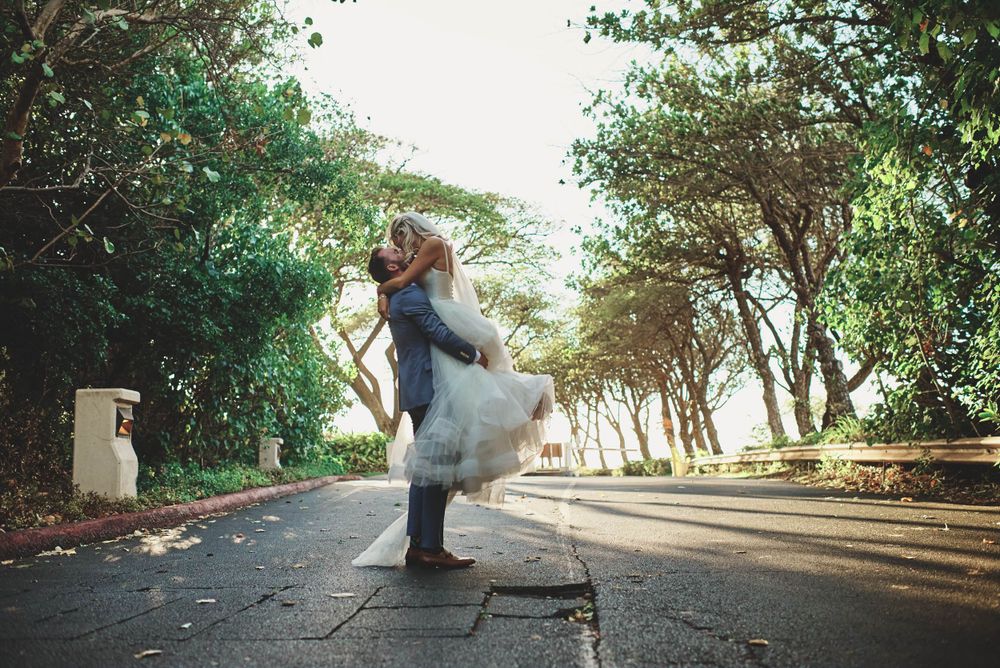 Joyful wedding couple dancing and twirling on a tree-lined path.