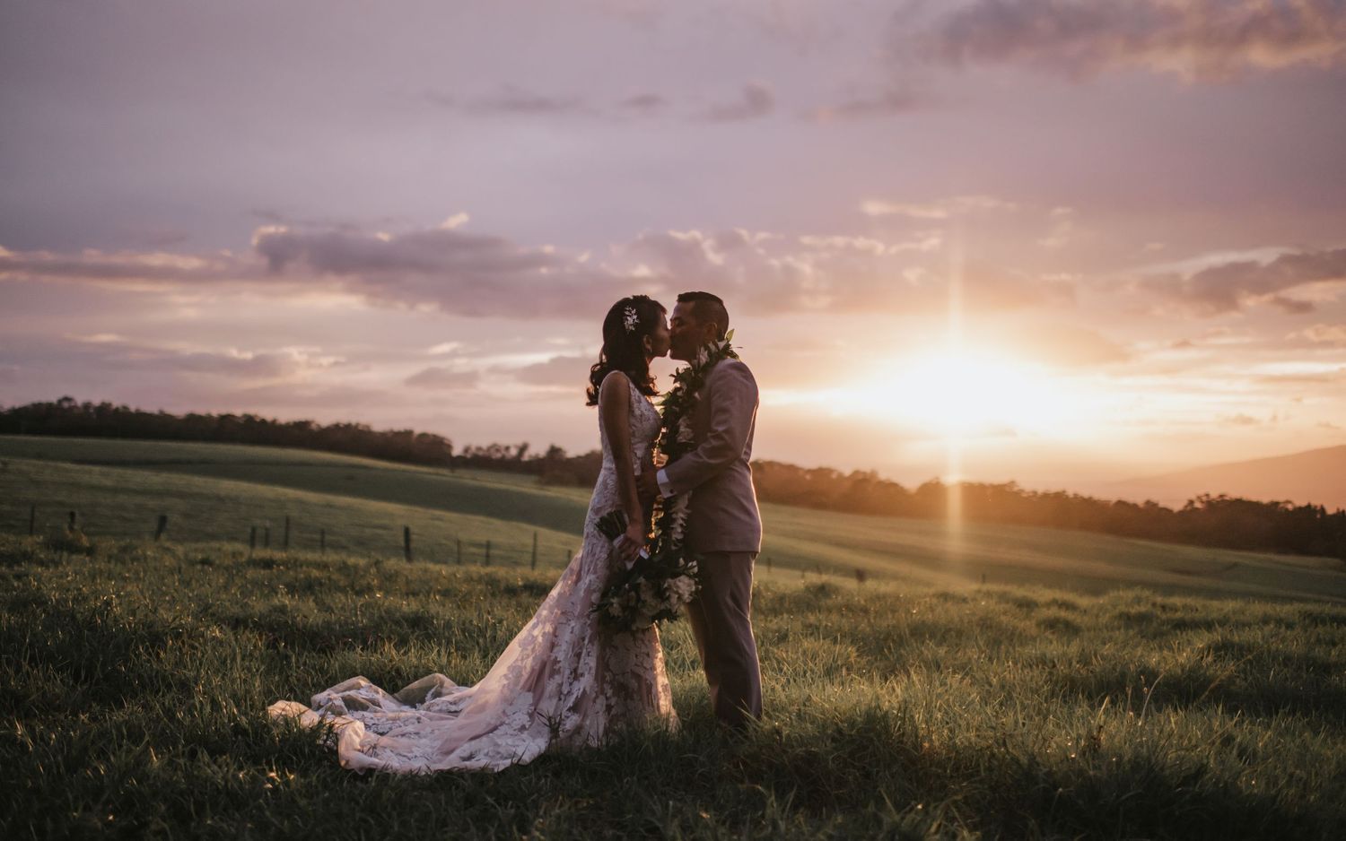 Romantic sunset silhouette of couple in grassy field with dramatic sky.