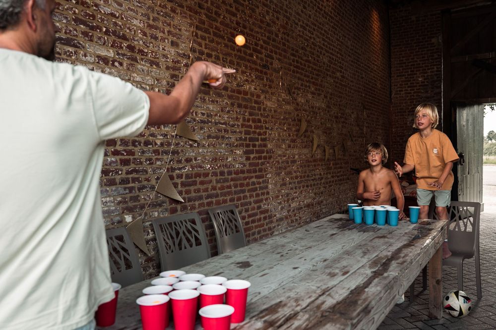 People playing cup pong on rustic wooden table against brick wall.