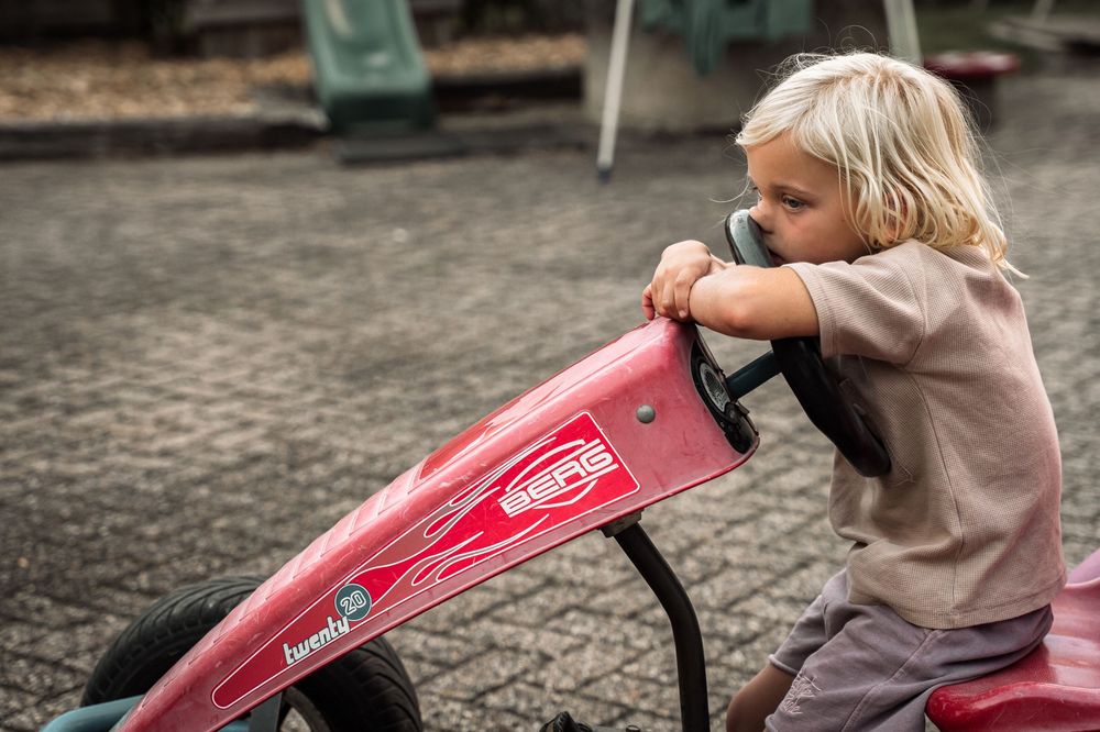 Child riding a bright red pedal go-kart on outdoor pavement.