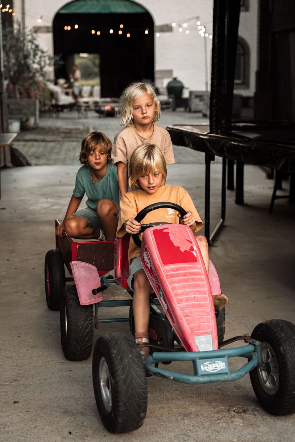 Children playing on a red pedal go-kart on a covered patio area.