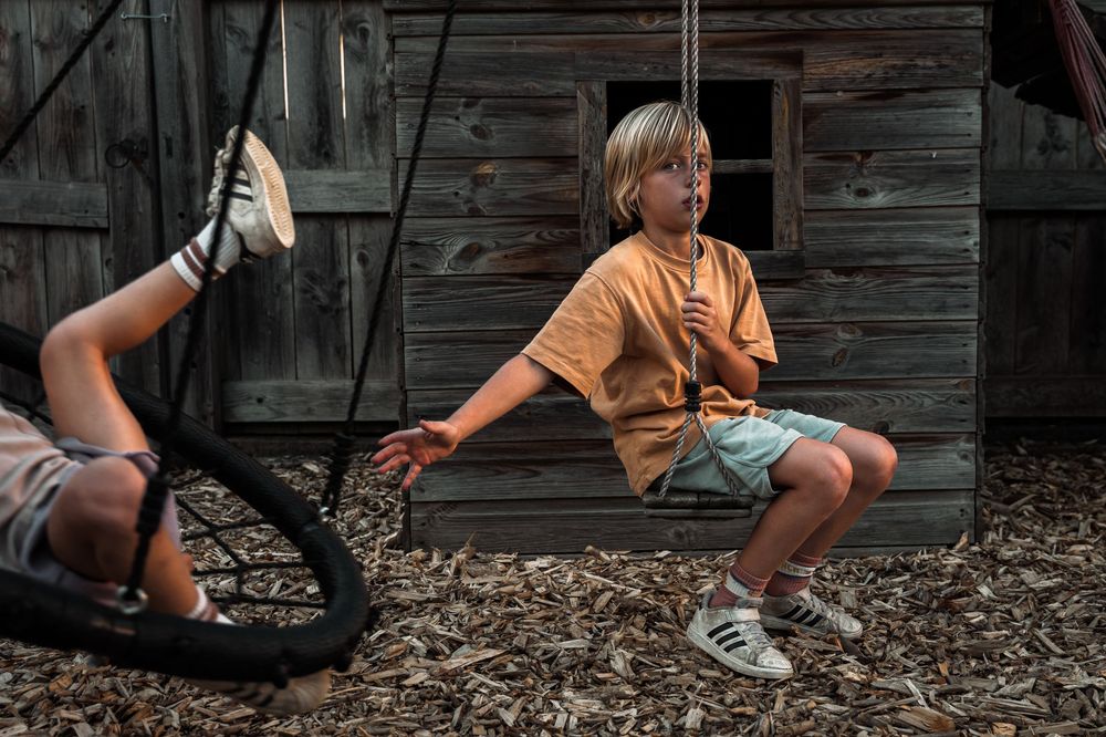 Children playing on outdoor playground equipment near a rustic wooden structure.