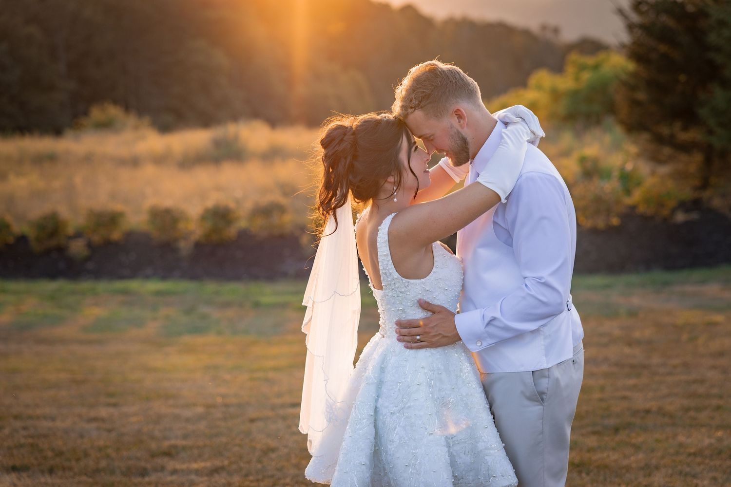 Sunset wedding portraits captured in warm golden light on a rural field.