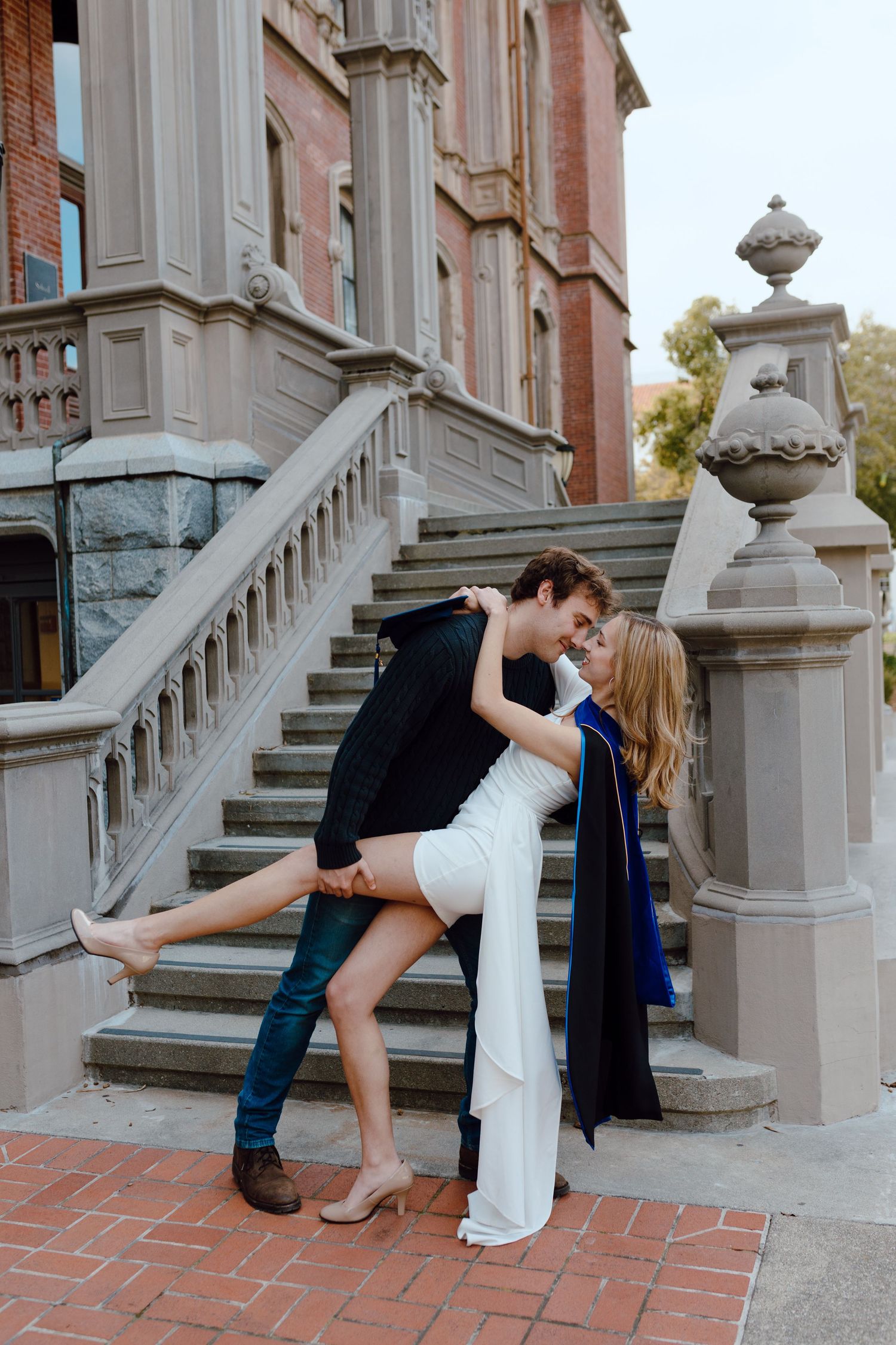 A couple graduating UC Berkeley together pose with a dip and kiss for their group graduation photoshoot.