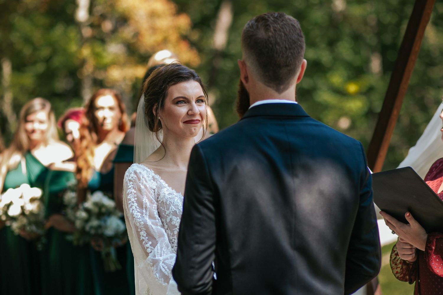 Outdoor wedding ceremony with couple at altar and bridesmaids in emerald green dresses.
