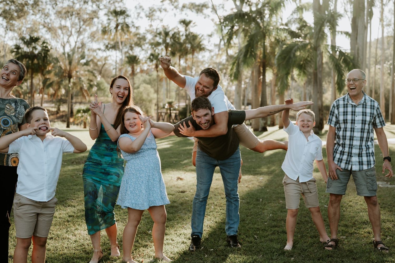 A joyful group poses together outdoors in a park with palm trees and natural lighting during golden hour.